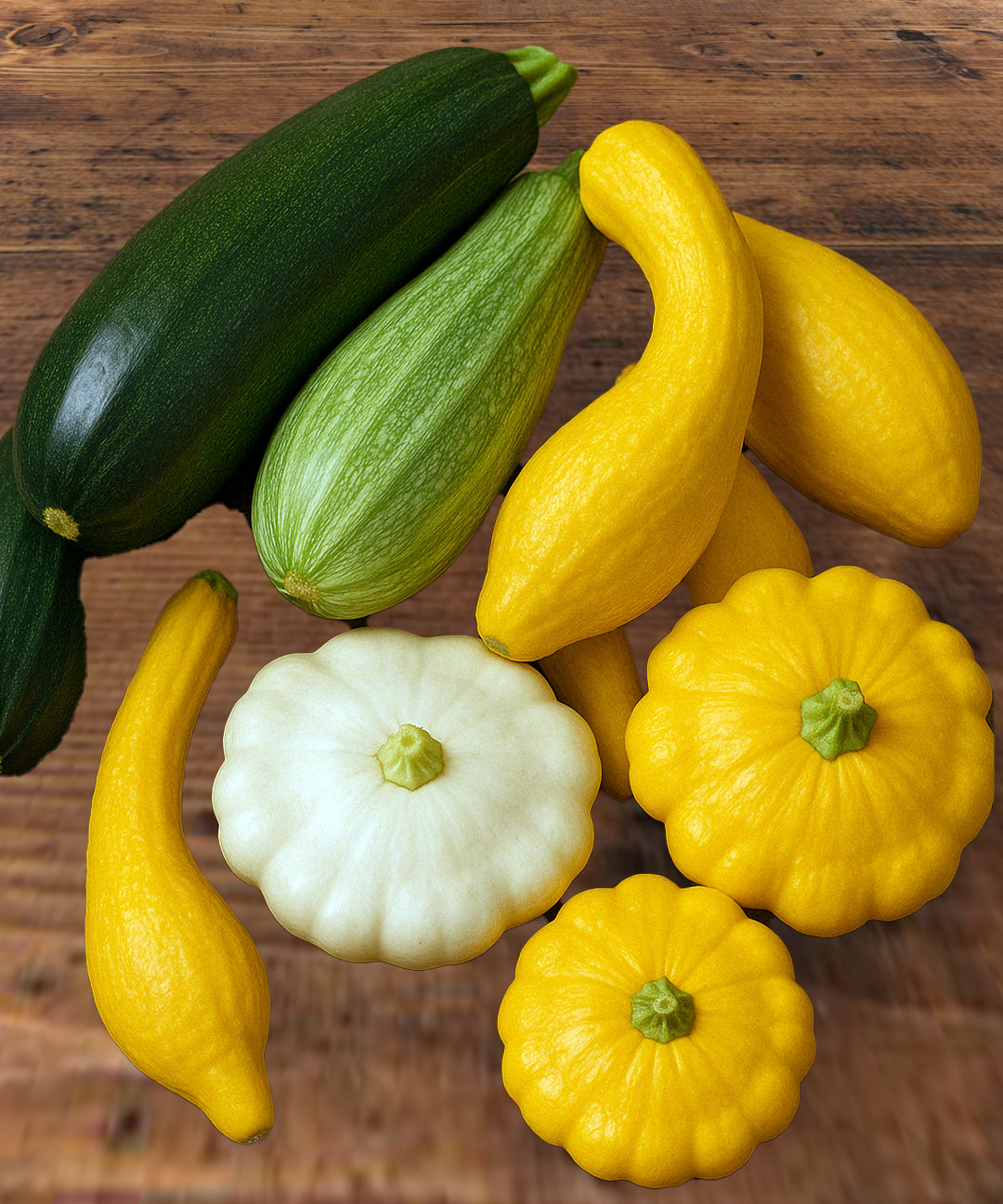 A freshly harvested assortment of heirloom summer squash varieties displayed on a rustic wooden table. Includes Black Beauty zucchini, striped Caserta zucchini, Early Summer Crookneck squash, White Scallop squash, and Yellow Scallop squash. The squashes are arranged in a casual pile, showcasing diverse shapes, textures, and colors. Ideal for garden seed listings, farm-to-table visuals, or vegetable product photography.